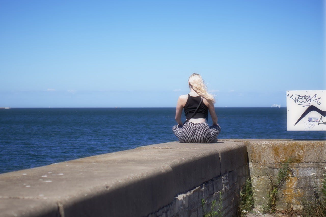 A girl is sitting alone on the seaside wall and enjoying the sea.