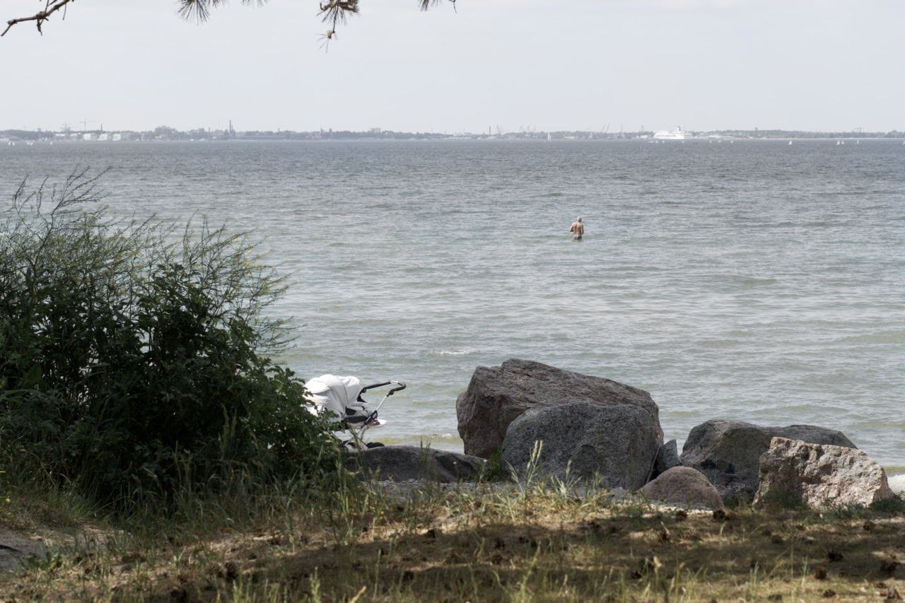 A baby in the stroller and an old man in the sea are enjoying the beach in Pirita, Tallinn. It's a summer day.