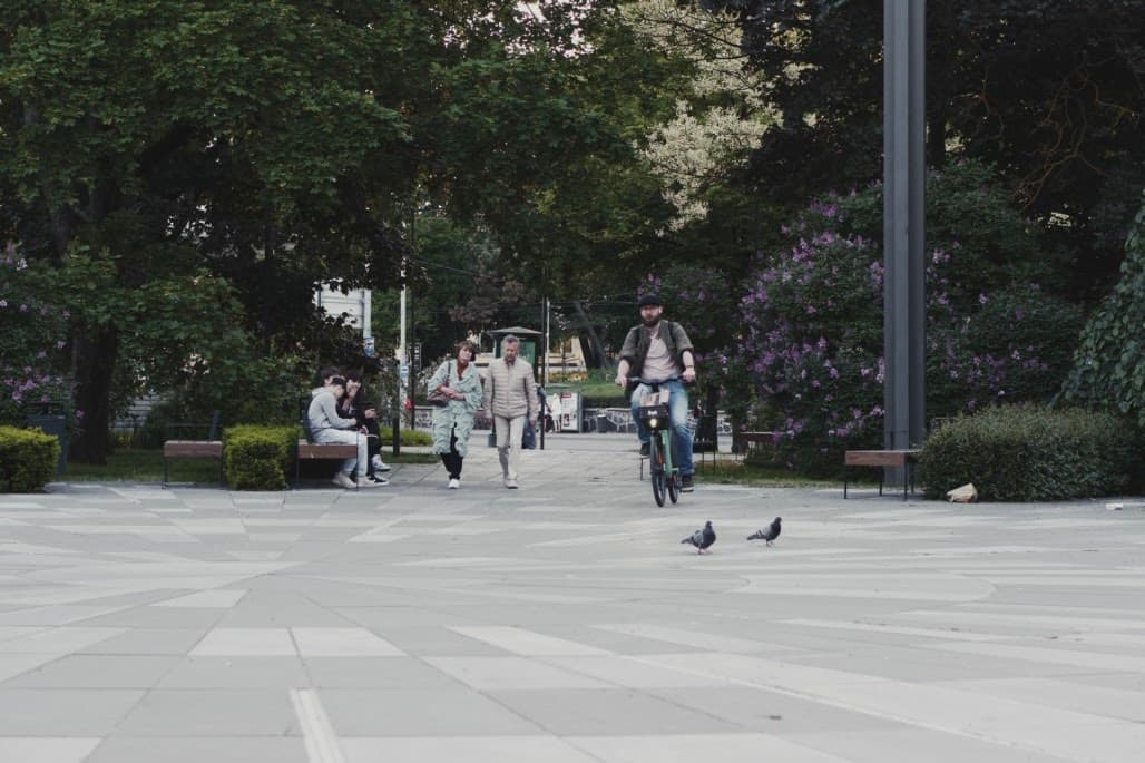 A couple of birds, a man with a bicycle, a couple of old people, and a group of friends are enjoying the summer night together in Taamsaare park, Tallinn.